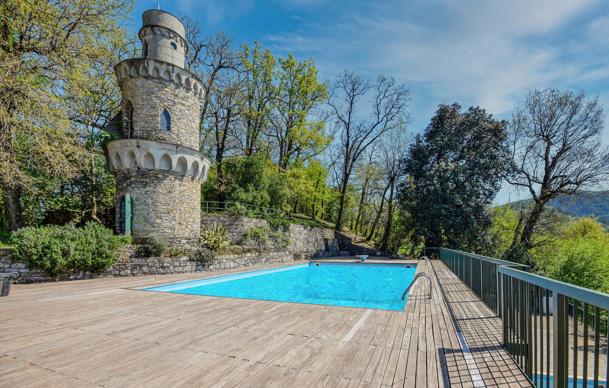 A castle-like structure with a swimming pool on a wooden deck, surrounded by trees and hills.