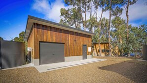 A modern building with a wooden facade, two garage doors, and a gravel driveway.