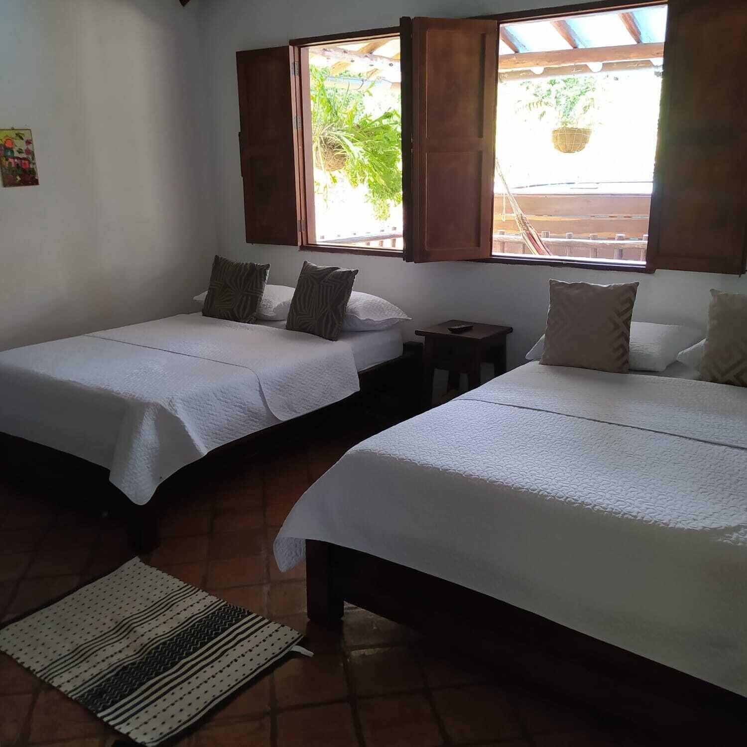 Una habitación con dos camas individuales, una mesita y una ventana con contraventanas abiertas.