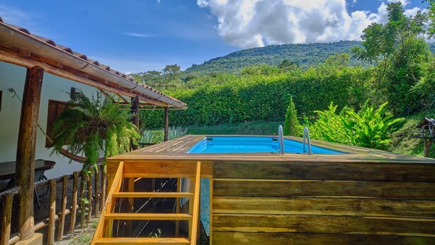 A wooden deck with a pool, surrounded by lush greenery and a mountain in the background. - Sueño Real Campestre Hostel (Pinchote)