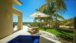 A pool area with a lounge chair and umbrella, a clear view of the ocean, and a well-maintained lawn. - Villa Oasis, a Luxury 6 BDR (San José del Cabo)