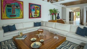 A modern living room with a white sofa, a wooden coffee table, and colorful abstract paintings on the wall. - Villa Oasis, a Luxury 6 BDR (San José del Cabo)