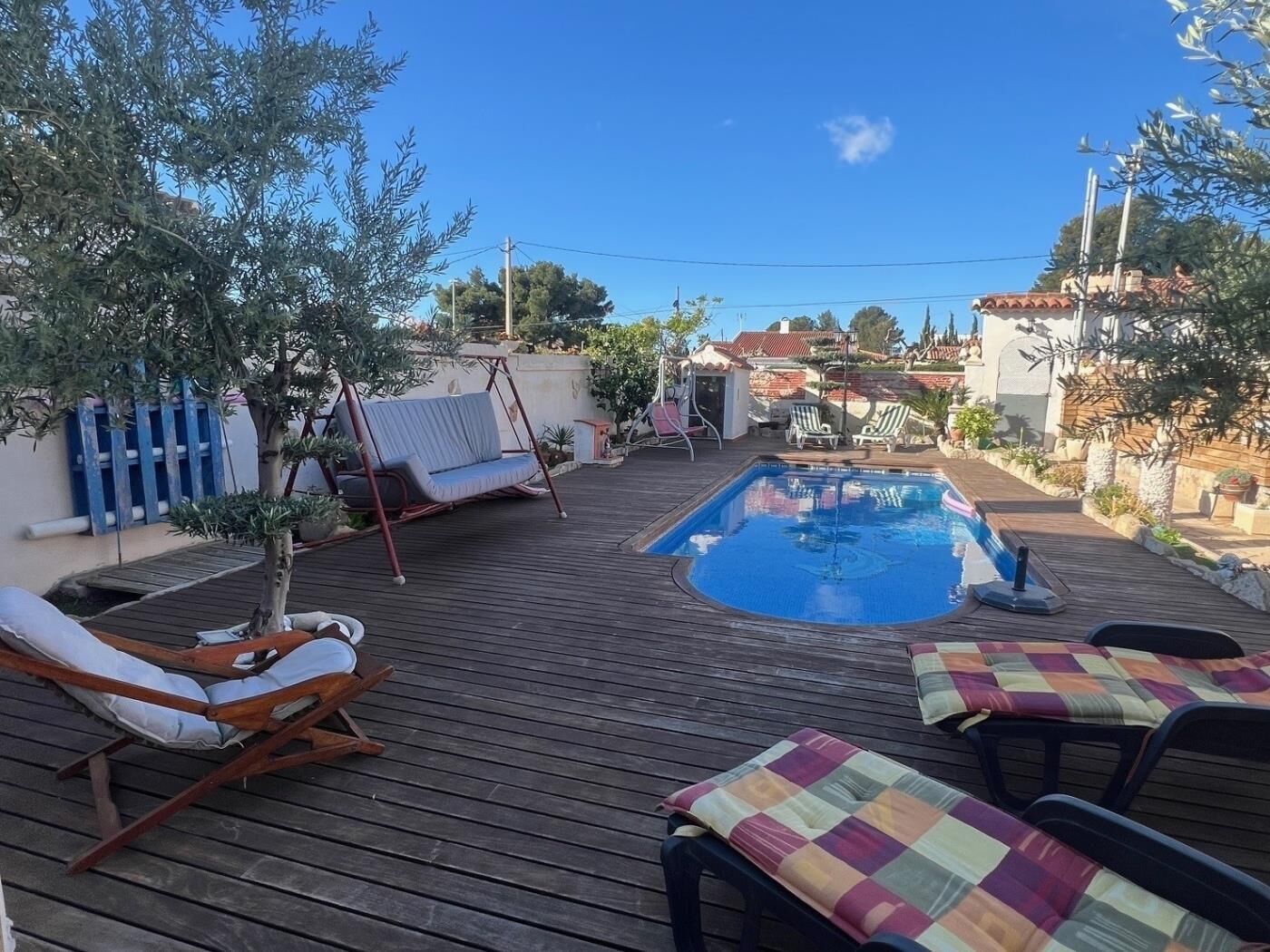 A wooden deck with a swimming pool, lounge chairs, and a swing chair.
