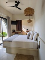 Un dormitorio con cama, ventilador de techo, televisor, lámpara colgante de mimbre y vistas al exterior.