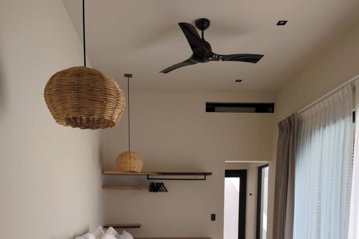 Ein modernes Schlafzimmer mit einem Bett, hängenden Korblampen, einem Deckenventilator und Blick ins Freie.