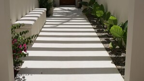 A white-walled corridor with a wooden door at the end, leading to a covered area. - Punta Mágica (Puerto Escondido)