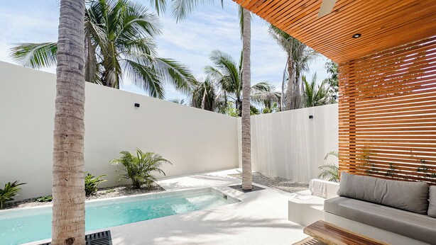 A modern outdoor pool area with a white wall, palm trees, and a wooden bench. - Punta Mágica (Puerto Escondido)