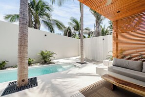 A modern outdoor pool area with a white wall, palm trees, and a wooden bench. - Punta Mágica (Puerto Escondido)
