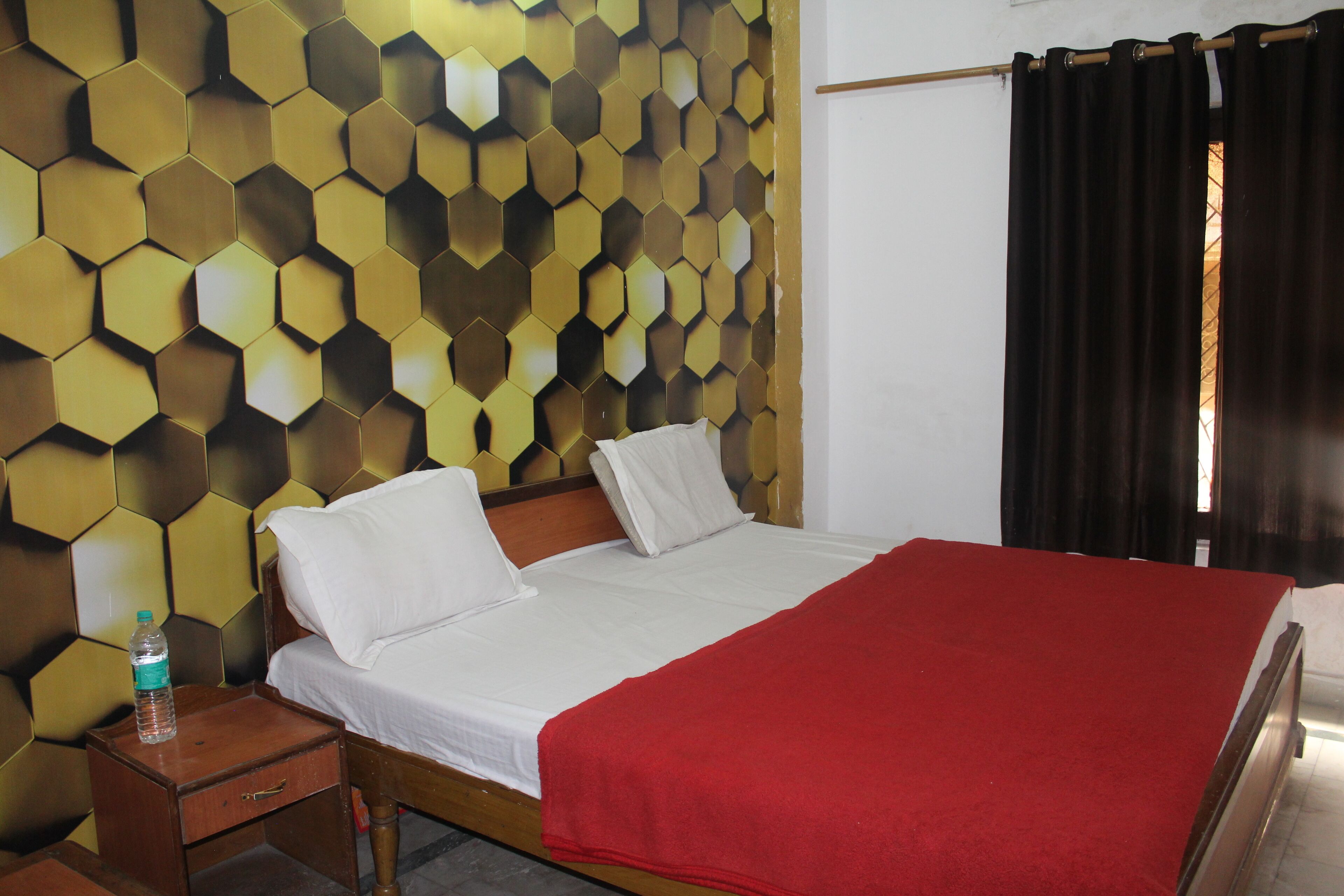 A hotel room with a bed, a wooden nightstand, a bottle of water, and a wall with a honeycomb pattern.