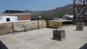 A rooftop with a concrete floor, a metal fence, and a view of a hilly landscape. - Shree Chitra Residency by Avadhesh Grou (Haridwar)