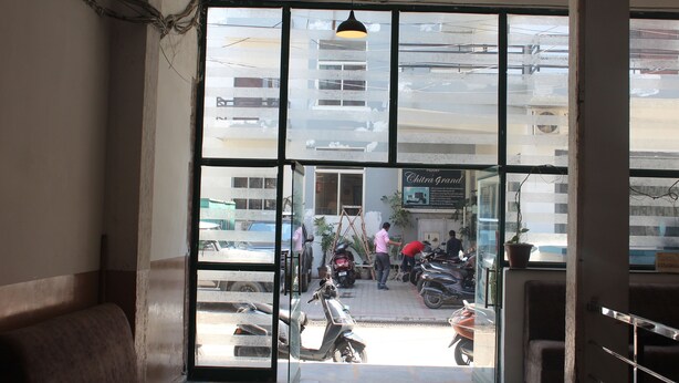 A view through a window with a metal frame, a hanging light fixture, and a bench inside a building. - Shree Chitra Residency by Avadhesh Grou (Haridwar)