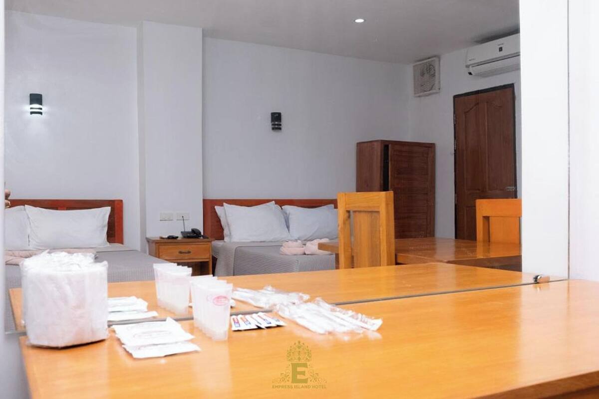 A hotel room with two beds, a wooden table with toiletries, and a mirror reflecting the room.