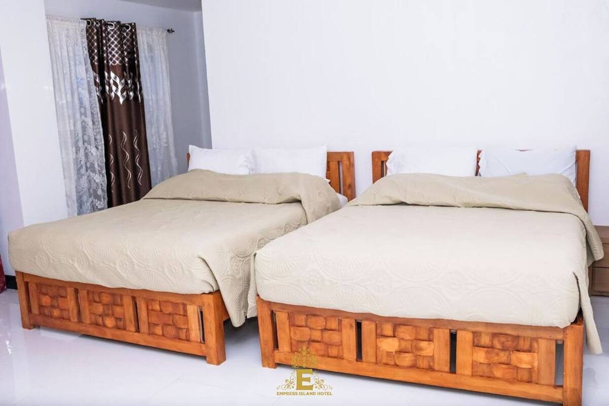 Two wooden beds with beige bedding in a hotel room.