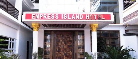 The entrance of the Empress Island Hotel with a prominent sign, a red carpet, and potted plants.