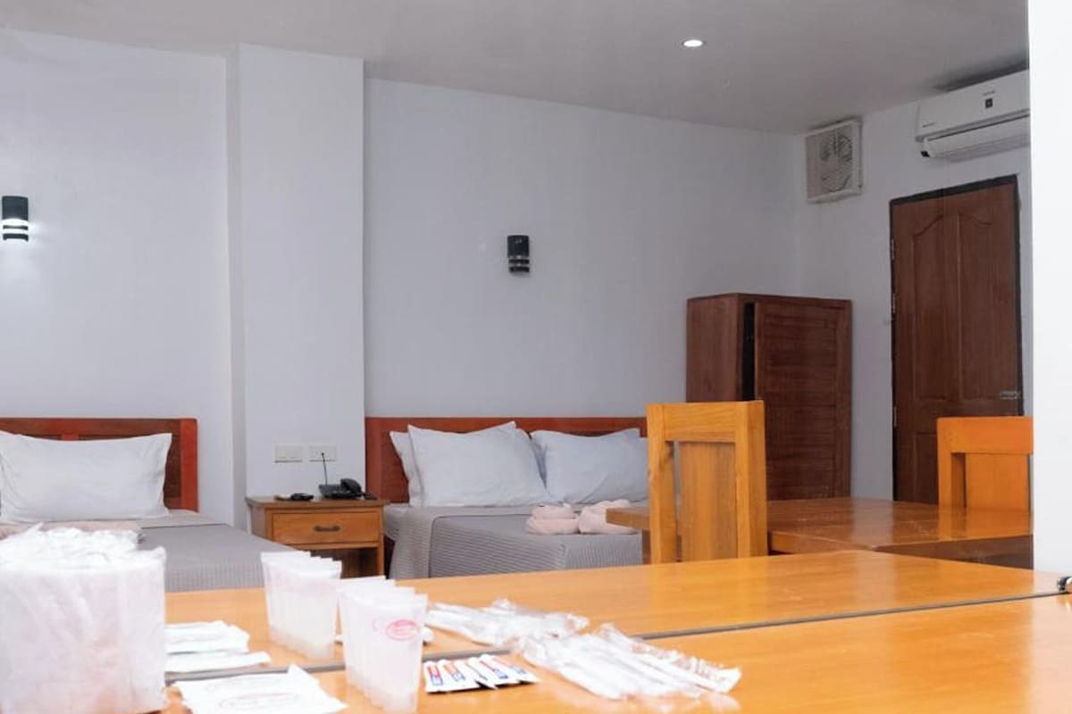A hotel room with two beds, a wooden table with toiletries, and a mirror reflecting the room.