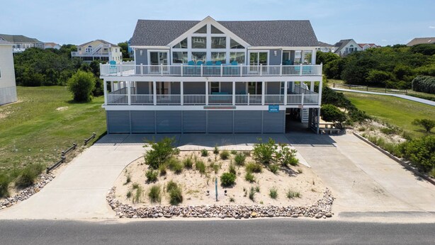 A two-story building with a balcony, a garage, and a landscaped area with rocks and shrubs.