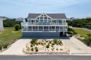 A two-story building with a balcony, a garage, and a landscaped area with rocks and shrubs. - A Golden Opportunity: Semi-Oceanfront w/Heated Pool, Hot Tub and Across from Beach! (Corolla)