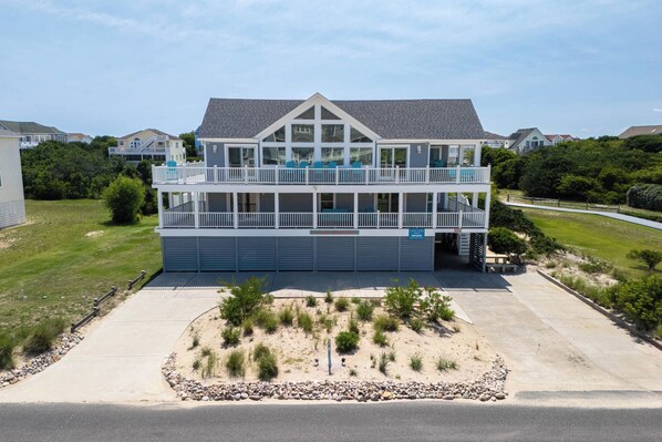 A two-story building with a balcony, a garage, and a landscaped area with rocks and shrubs.