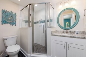 A modern bathroom with a glass-enclosed shower, a white toilet, a vanity with a marble countertop, and a round mirror with a teal frame.