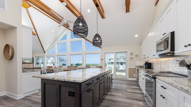 A spacious kitchen with a large island, dark cabinetry, and a view to the outside. - A Golden Opportunity: Semi-Oceanfront w/Heated Pool, Hot Tub and Across from Beach! (Corolla)