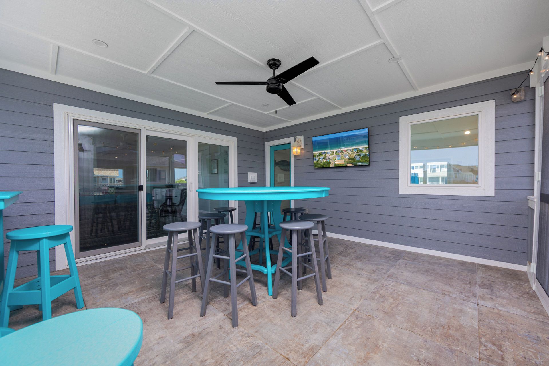 A covered patio area with a table and chairs, a ceiling fan, and a TV mounted on the wall.