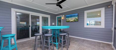 A covered patio area with a table and chairs, a ceiling fan, and a TV mounted on the wall.