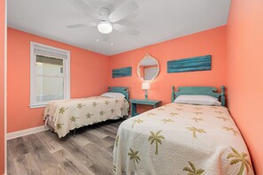 A bedroom with two beds, a ceiling fan, a window, and artwork on the walls. - A Golden Opportunity: Semi-Oceanfront w/Heated Pool, Hot Tub and Across from Beach! (Corolla)