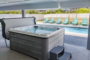 A hot tub with a wooden exterior, a pool with blue lounge chairs, and a view of a residential area. - A Golden Opportunity: Semi-Oceanfront w/Heated Pool, Hot Tub and Across from Beach! (Corolla)