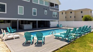 A two-story house with a backyard pool, deck chairs, and a hot tub.