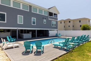 A two-story house with a backyard pool, deck chairs, and a hot tub.