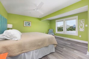 A bedroom with a bed, a ceiling fan, a window with a view, and a chair. - A Golden Opportunity: Semi-Oceanfront w/Heated Pool, Hot Tub and Across from Beach! (Corolla)