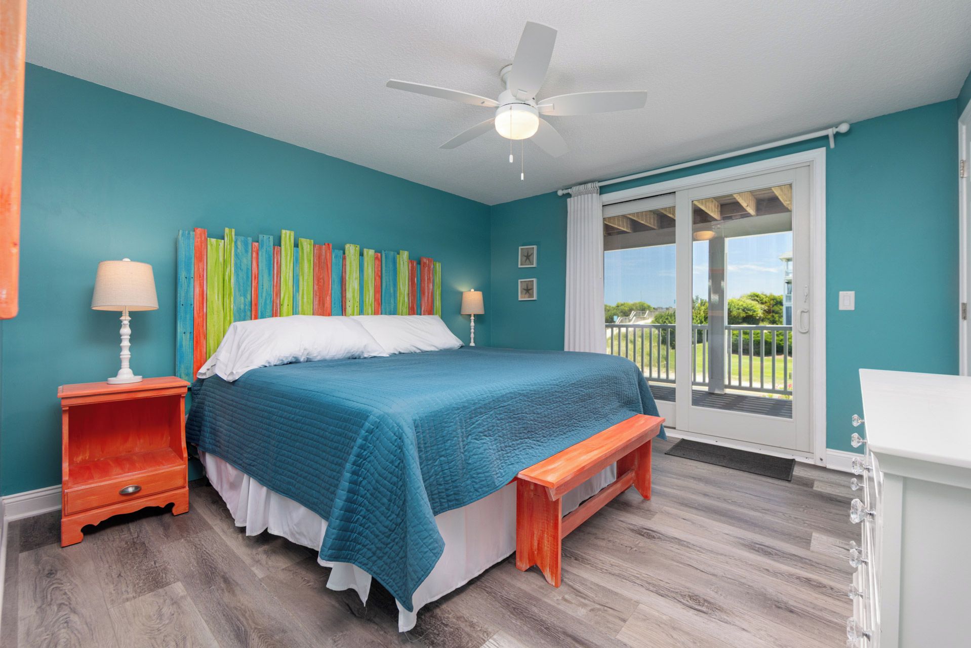 A bedroom with a bed, a ceiling fan, a window with a view, and a wooden bench.