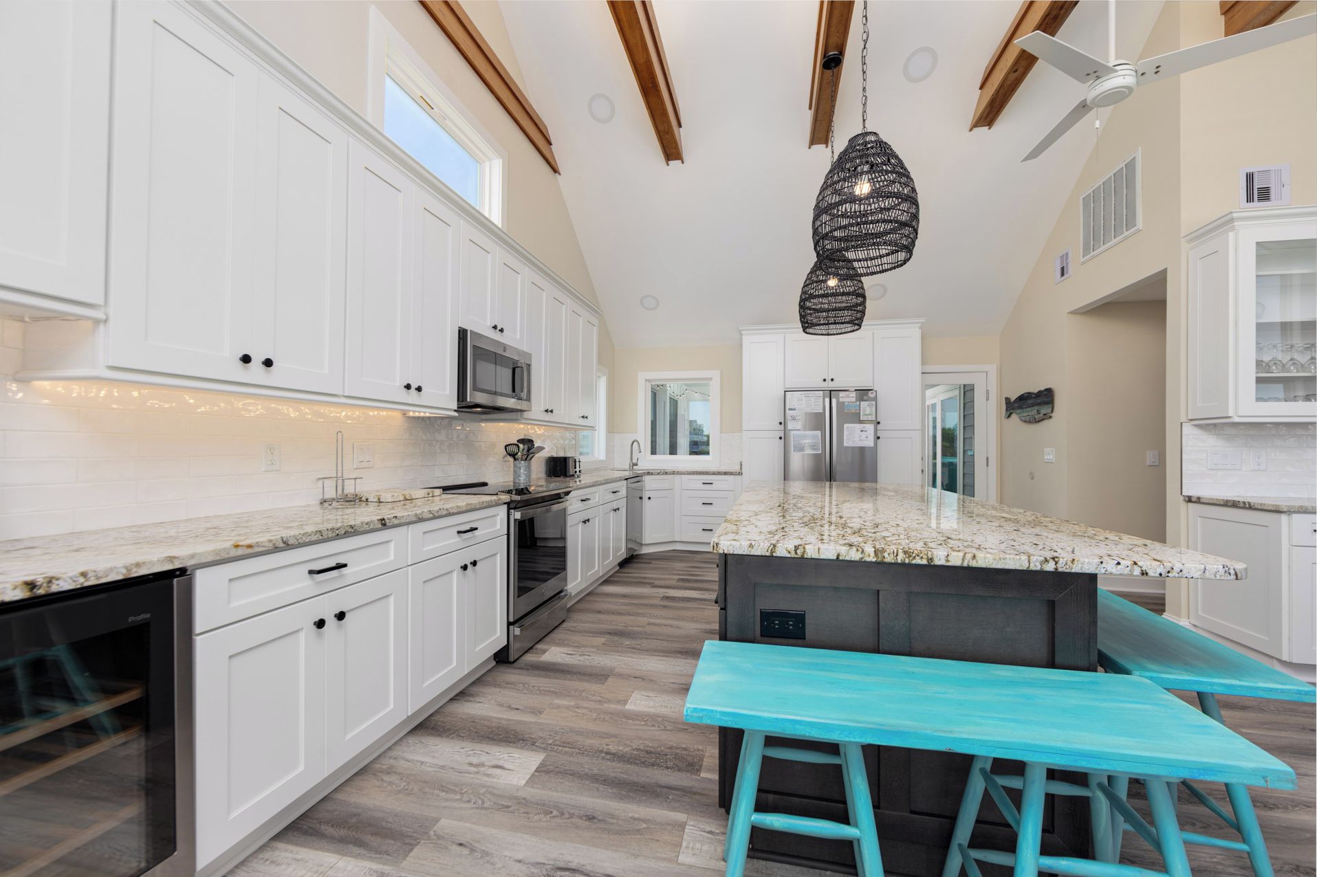A modern kitchen with white cabinets, a large island, and a teal bench.