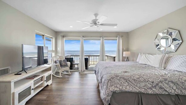 A bedroom with a large bed, a TV, a ceiling fan, and a view of the ocean. - Beachfront Beauty w/ Hot Tub ~ 10 Steps to Sand (Galveston)