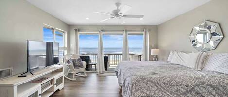 A bedroom with a large bed, a TV, a ceiling fan, and a view of the ocean.