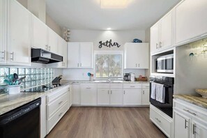 A modern kitchen with white cabinets, a black stove, and a window with blinds.