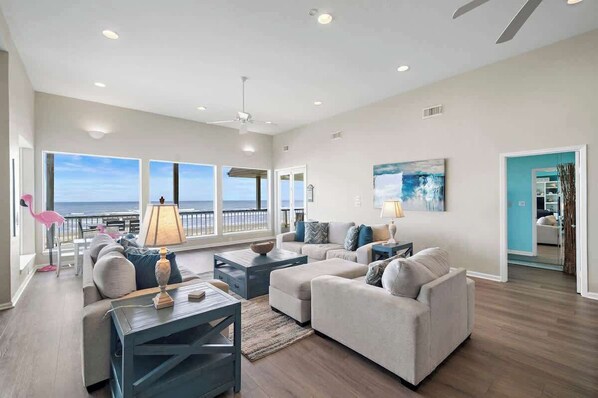 Ein geräumiges Wohnzimmer mit großem Fenster zum Meer, Deckenventilator und modernem Interieur.