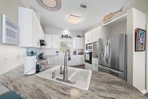 A modern kitchen with white cabinets, a stainless steel refrigerator, and a marble countertop.