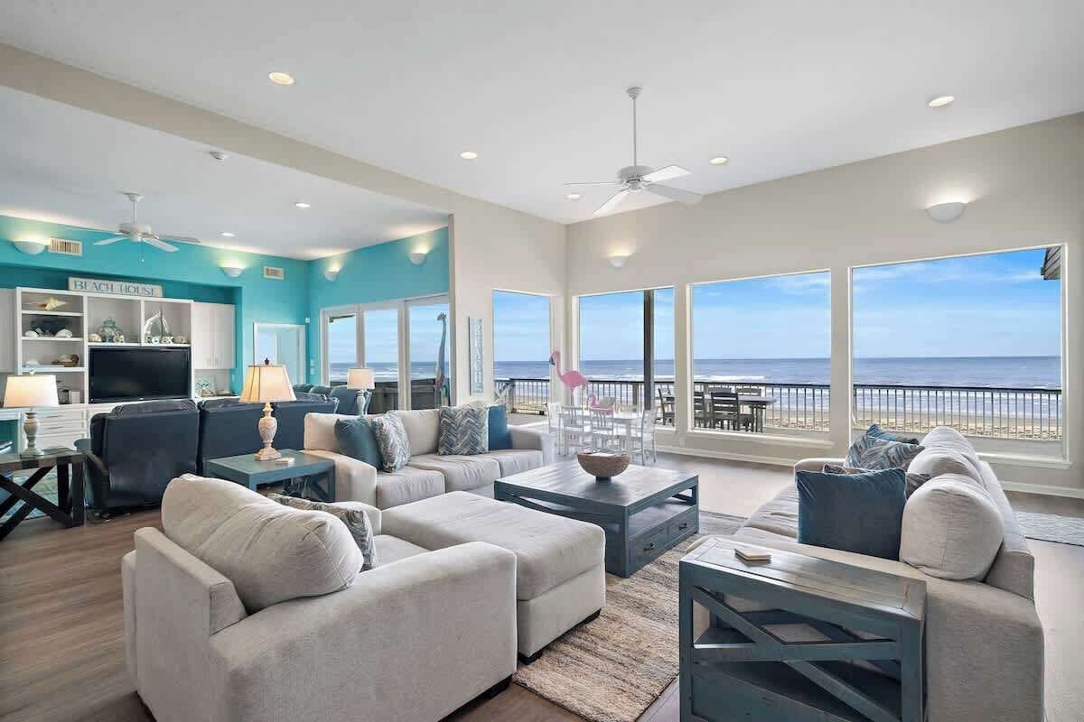 A spacious living room with a large TV, comfortable seating, and a view of the ocean.