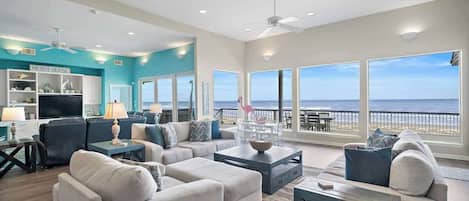 A spacious living room with a large TV, comfortable seating, and a view of the ocean.