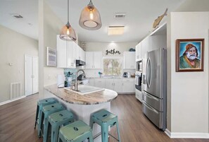 A modern kitchen with white cabinets, a central island with stools, a stainless steel refrigerator, and pendant lighting.