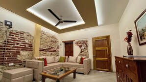 A living room with a sectional sofa, a glass-top coffee table, a ceiling fan, exposed brick walls, and a wooden door. - Casa Stephanie- Prívate Pool (Cartagena de Indias)