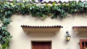 A building with a wooden door, steps leading to the entrance, a wall-mounted lantern, and a potted plant to the left. - Casa Stephanie- Prívate Pool (Cartagena de Indias)