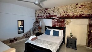 A bedroom with a bed, a nightstand, a ceiling fan, and a brick wall. - Casa Stephanie- Prívate Pool (Cartagena de Indias)