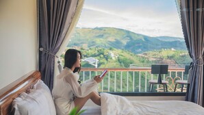 A person sitting on a bed in a room with a view of green hills.