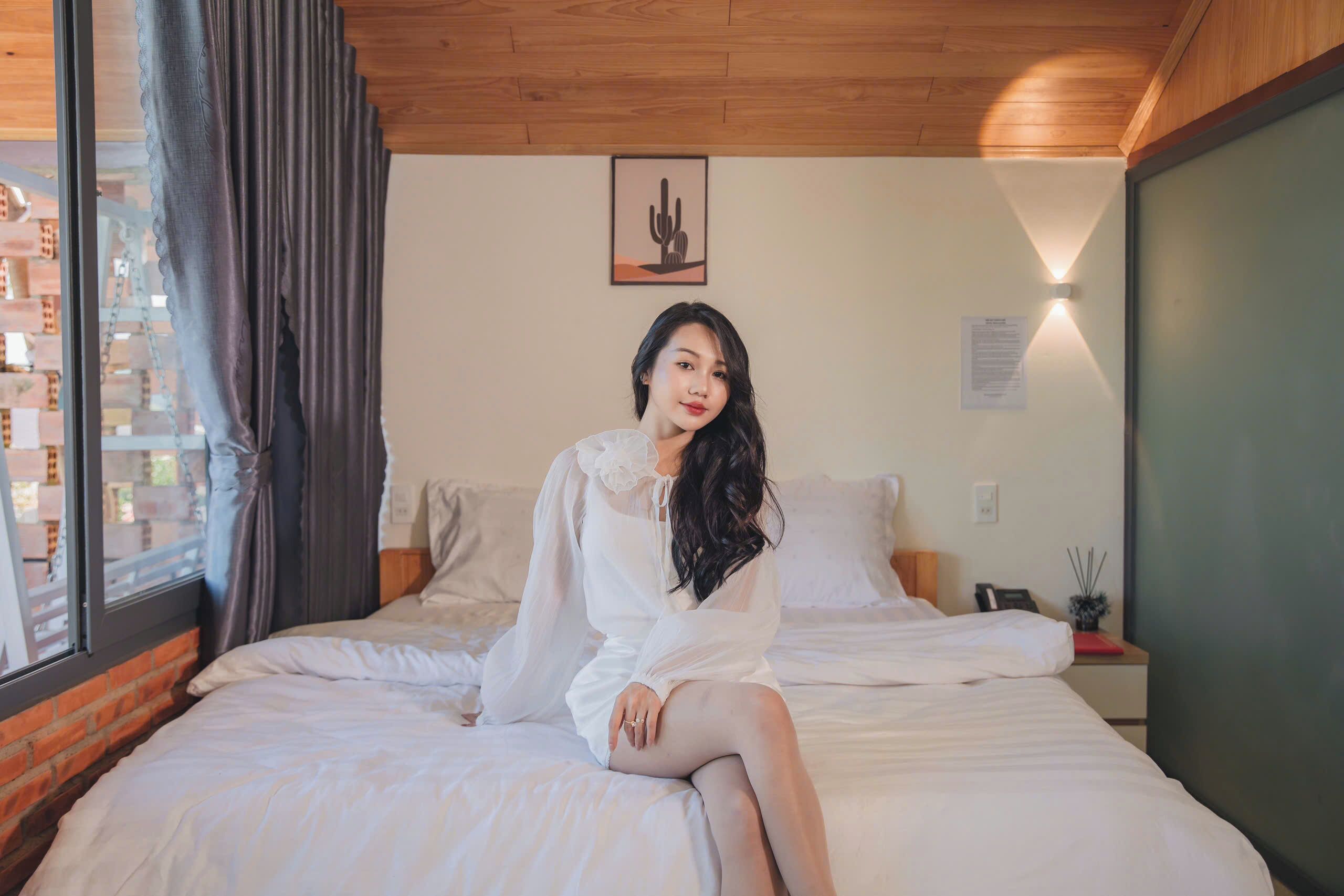 A room with a bed, a window with curtains, a cactus artwork on the wall, and a nightstand with a lamp.