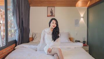 A room with a bed, a window with curtains, a cactus artwork on the wall, and a nightstand with a lamp.