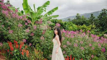 A woman in a dress standing in a garden with various plants and flowers.
