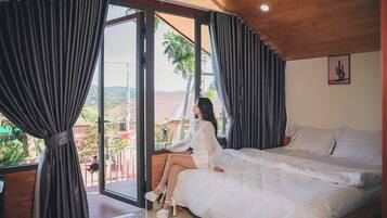 A bedroom with a large bed, a view of the outdoors, and a balcony.