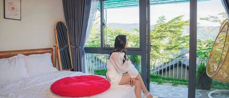 A room with a bed, a large window, and a view of greenery outside.